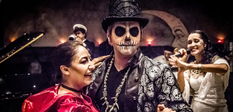 Close-up photo of a group of people in Halloween costumes, with a couple dancing in the foreground and a singer with her band visible in the background.